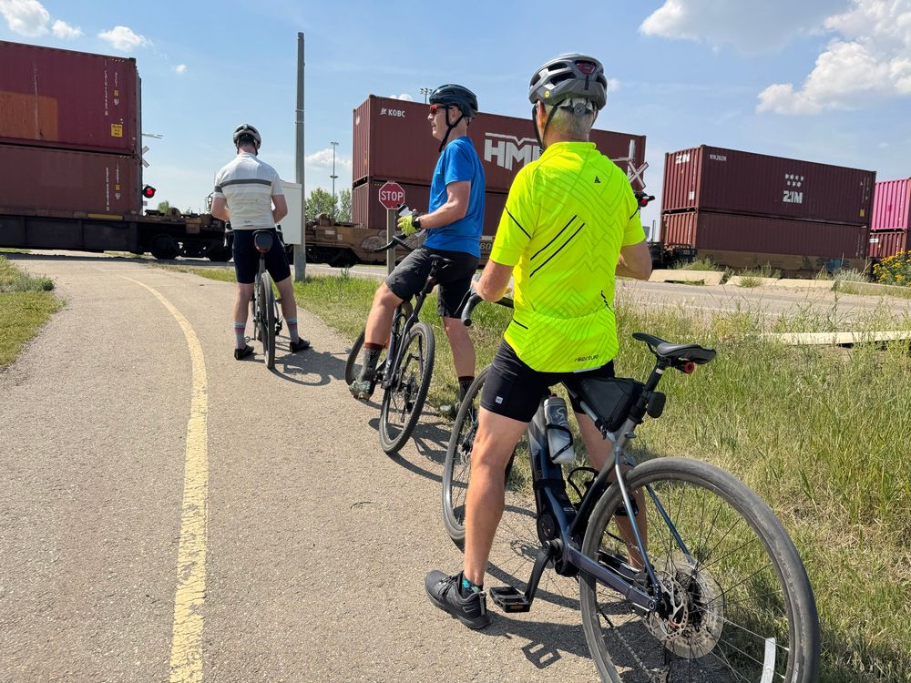 Three cyclists wait for train at crossing 