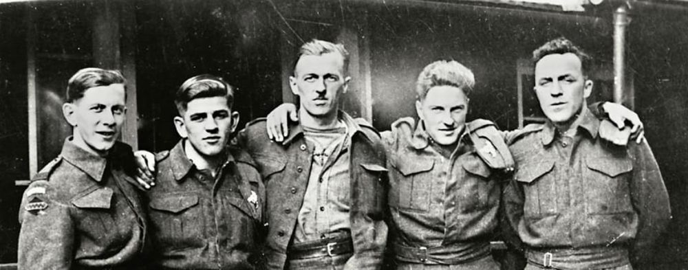 5 soldiers, arms over shoulders of their fellow soldiers 