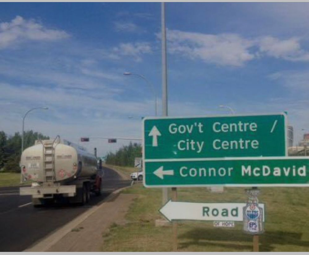 tanker truck driving by altered green traffic sign 