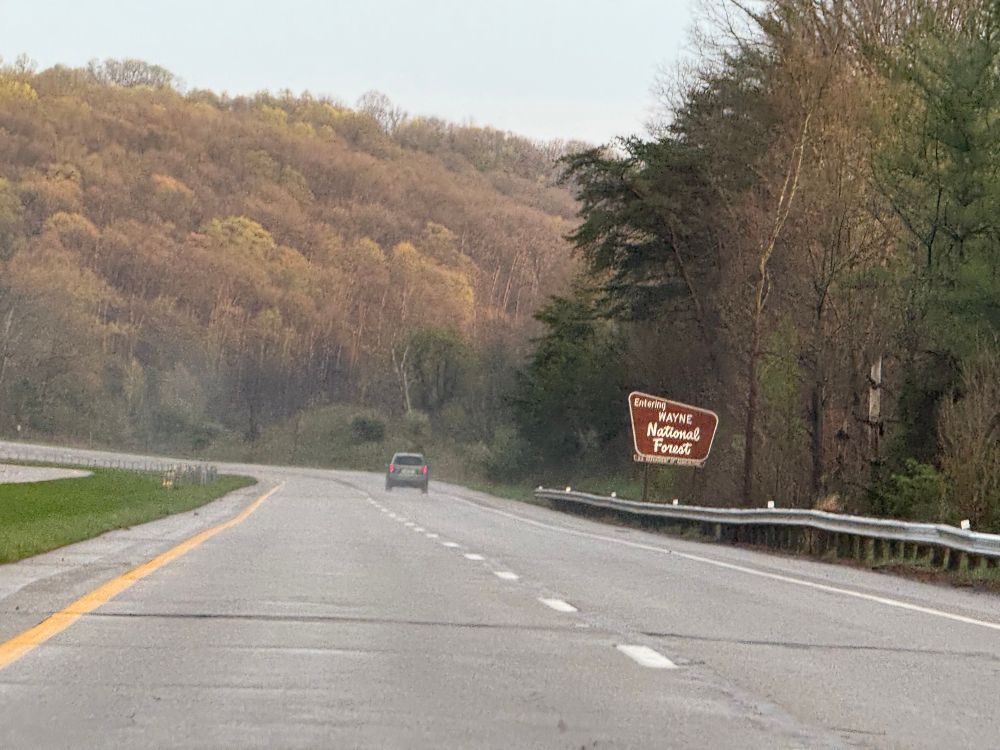 A highway in southeast Ohio. The brown sign to the right reads “Entering Wayne National Forest”. There are tree covered hills surrounding the highway 