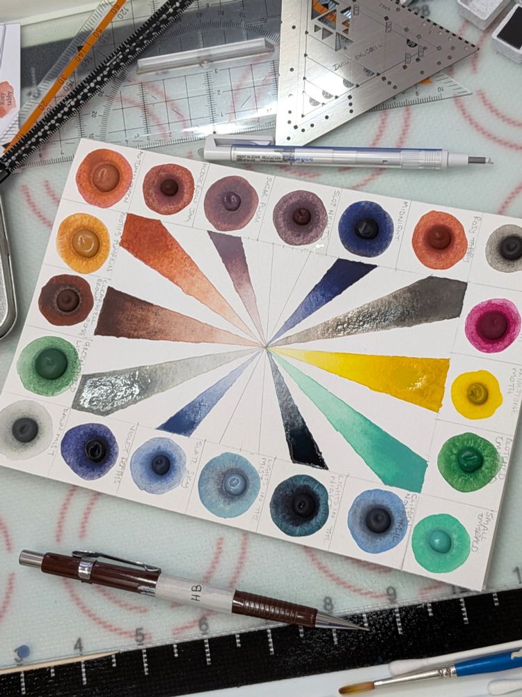 The card being made on my work bench. Alternate rays have been coloured in and are drying. Around the card are rulers and set squares, pencils, an eraser and a paintbrush. Y'know the usual mayhem.