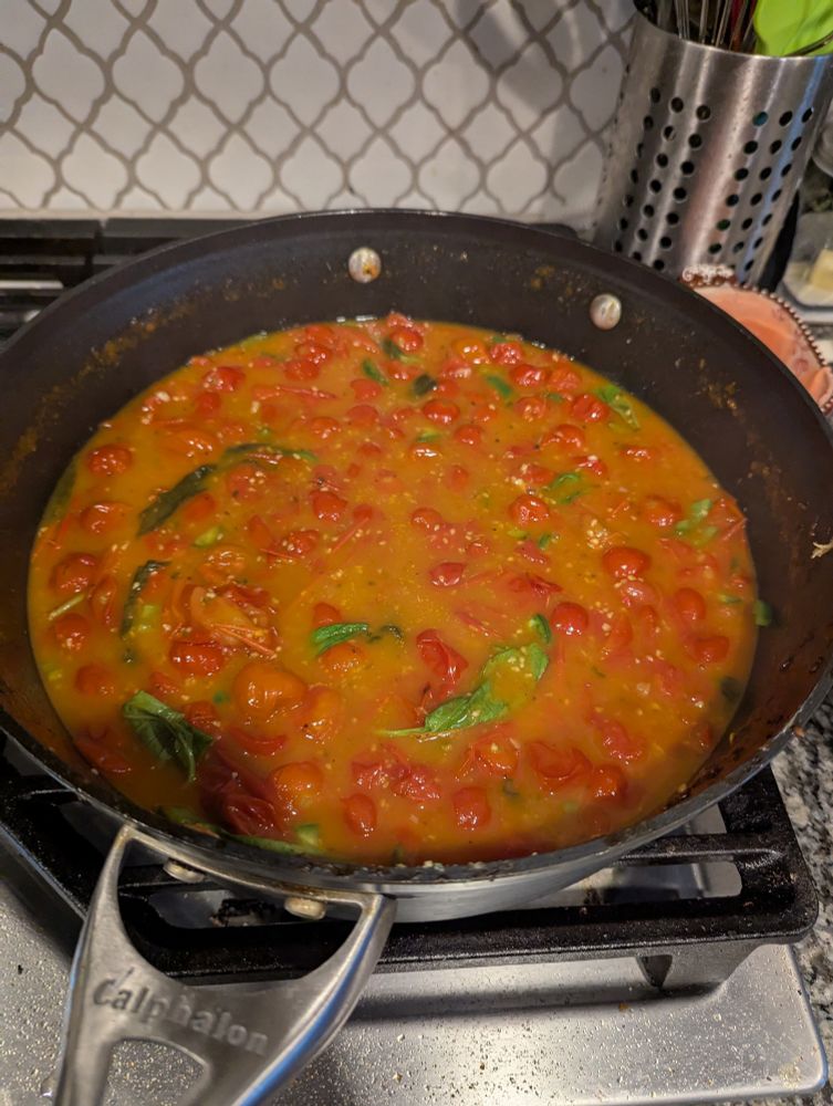 A pan of tomatoes and basil simmers on the stove