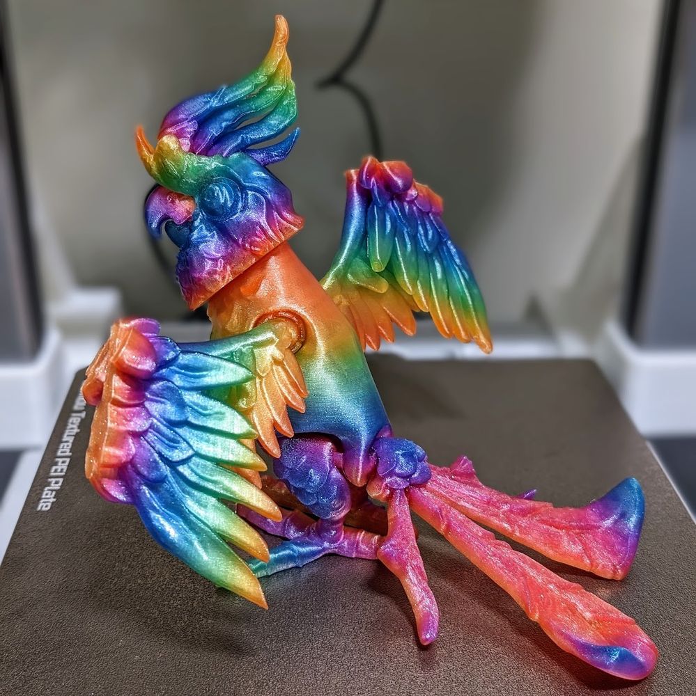 3d printed cockatoo by twisty prints in a glitter rainbow filament standing wings closed from the back