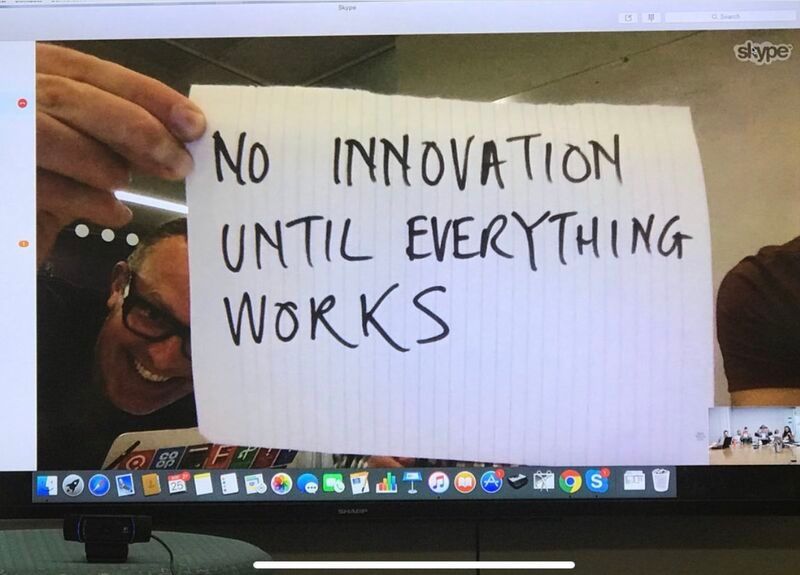A guy on a Zoom call holding a paper up to the camera that says, no innovation until everything works. 