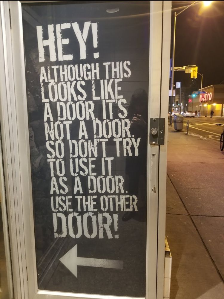 A glass door has a full-size poster inset behind the glass that says, Hey! Although this looks like a door it's not a door, so don't try to use it as a door. Use the other door!