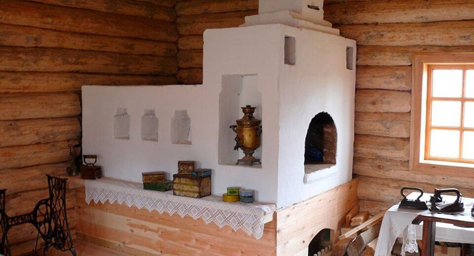 Vintage Russian-style whitewashed brick oven in a log cabin with a Samovar on the side