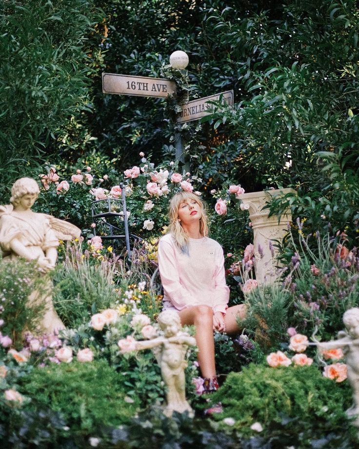 Taylor Swift from the Lover photoshoot with flowers surrounding her in a garden. There is a street sign that says 16th ave and cornelia street. 