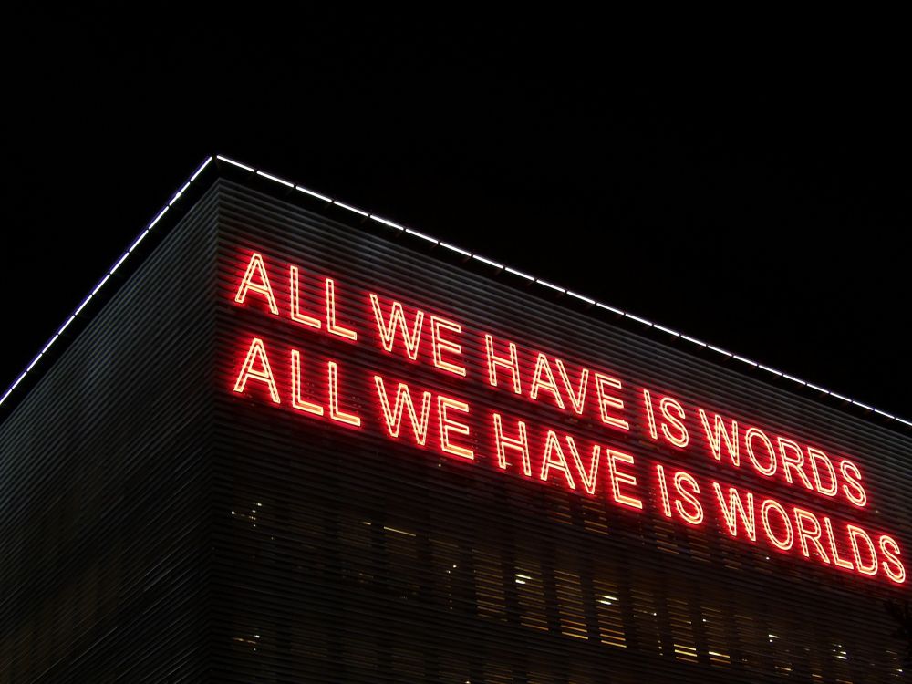 Huge building with neon letters in all capitals: all we have is words; all we have is worlds
