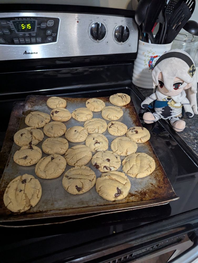 A corrin plush next to a fresh tray of chocolate chip cookies 