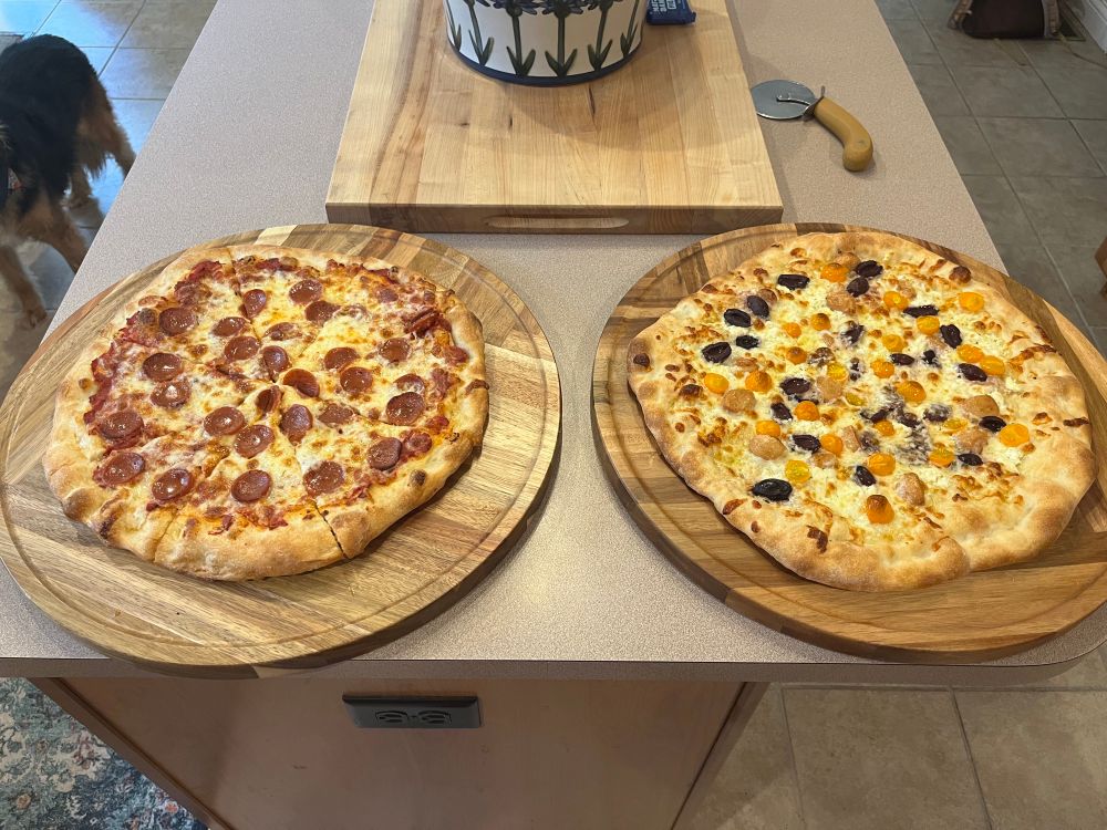 Homemade pepperoni pizza and another with olive, tomato, roasted garlic, and goat cheese 