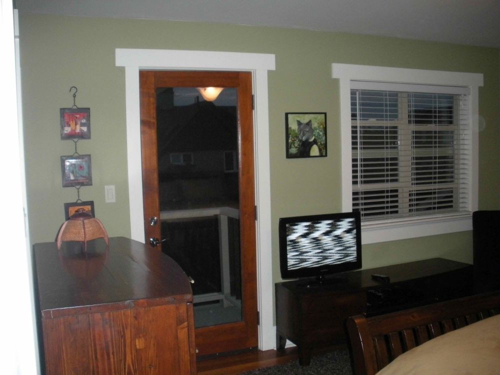IMAGE OF WALL INSIDE HOUSE. THERE IS A WOODEN INSIDE DOOR LEFT OF CENTRE. NEXT TO THE DOOR IS A FLAT SCREEN TV SHOWING STATIC. A SQUARE PAINTING OF A CAT WEARING HUMAN CLOTHES IS ON THE WALL ABOVE THE TV. IT IS DARK OUTSIDE.