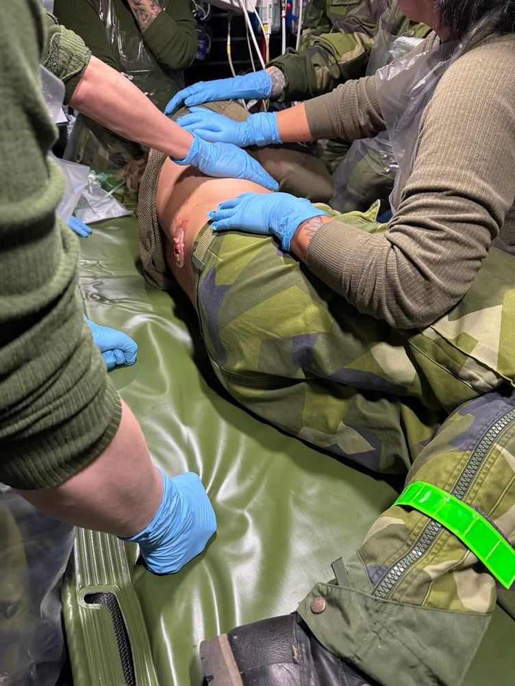 En sårad figurant ligger på en brits, han har ett fejkat skottsår på ryggen. Runt om står fem sjukvårdare 