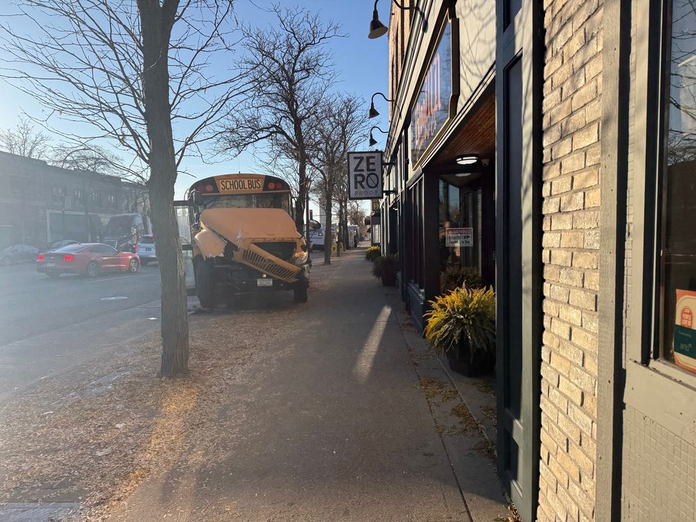A school bus with a wrecked front end rests partially on the sidewalk