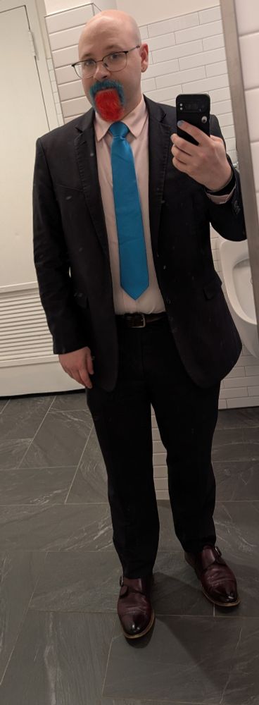 Sorry but it's literally just a picture of me and the implication is that I look younger than he does but it's more of a gestalt thing, if it helps I'm wearing a dark grey suit with red-brown shoes, a pink shirt and a teal tie; my head is clean-shaven and I have a pink and turquoise guard.  It's a mirror selfie taken in a courthouse bathroom.