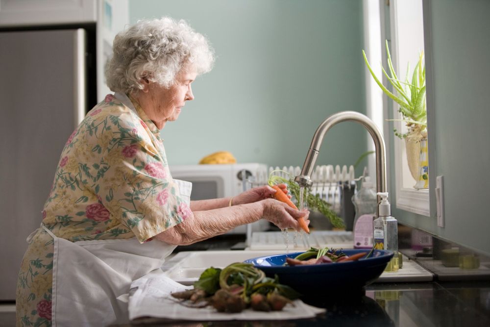 Woman wearing yellow and pink floral dress washing carrots. 