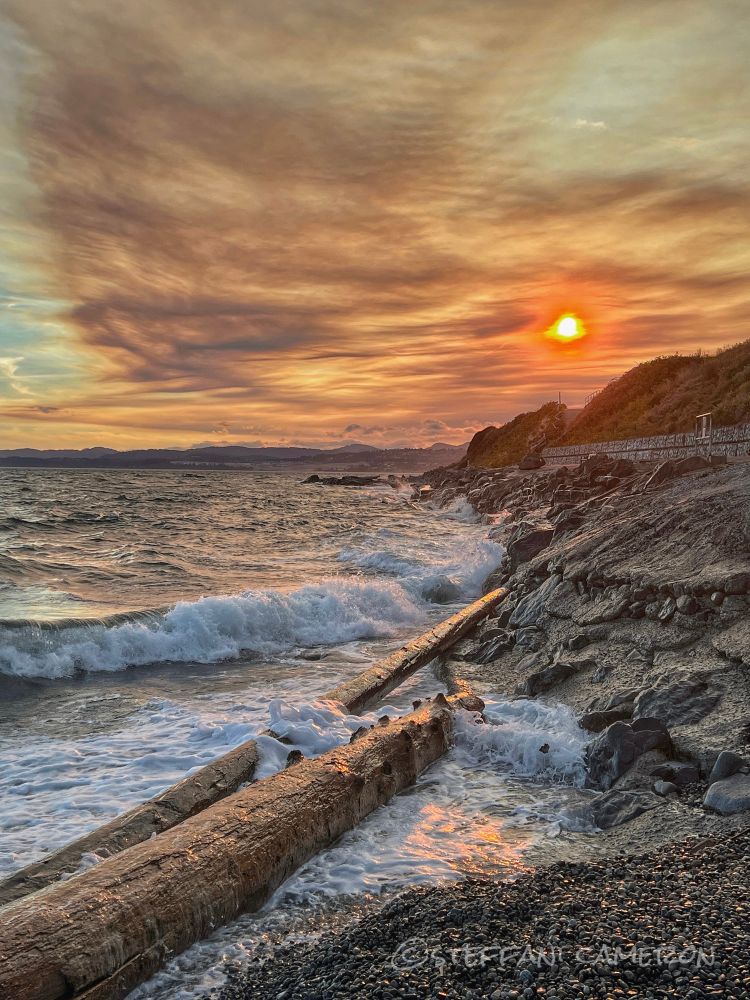 An orange wildfire sunset by the sea at high tide in wind with big waves