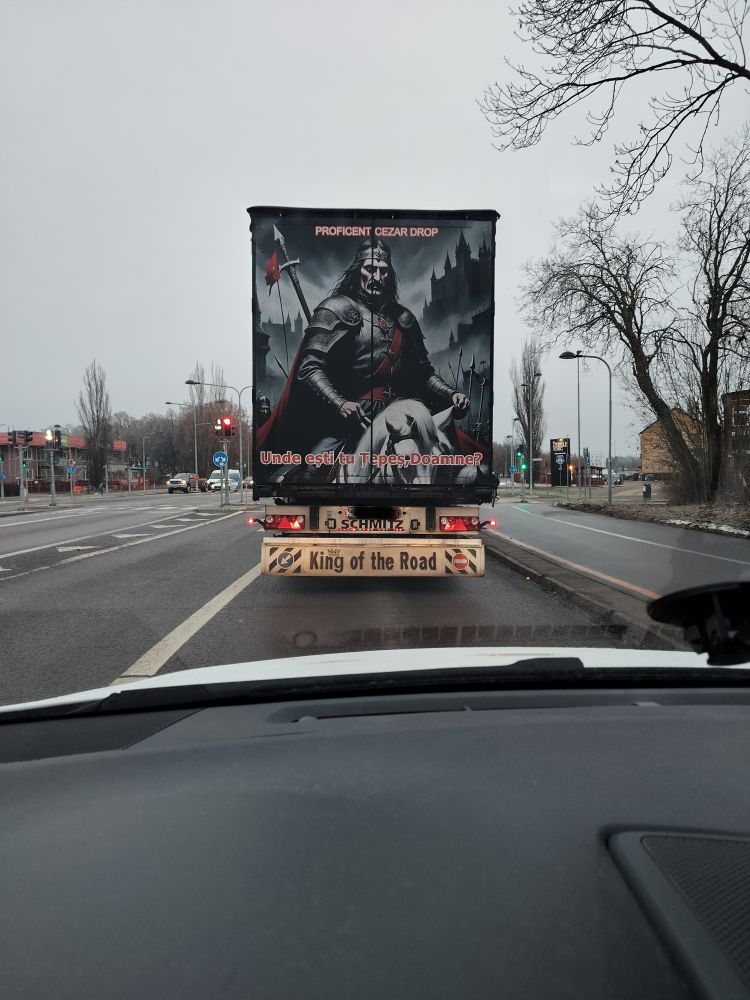 A picture of the back of a truck taken from another car at a traffick light. 
There is a big poster on the doors from the back of the truck depicting a Romanian historical character, Vlad the Impaler, a local ruler from Valahia from the 15th century. In popular culture, due to Bram Stoker's fantasy novel Dracula, he is associated with this fictitious character.
He was a despot, like many rulers of his time, known for impaling people who were uncomfortable for him. A nationalistic rewriting of history portrays him as impaling those who were dishonest. 
