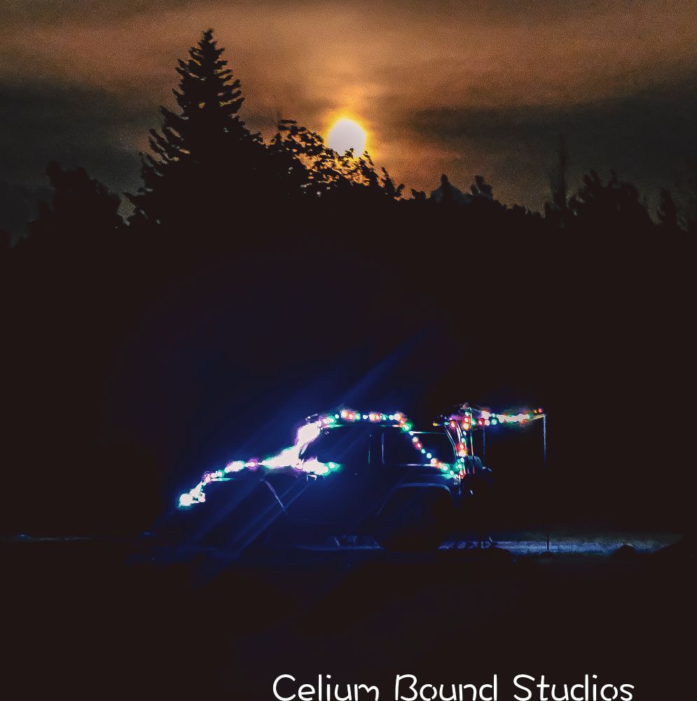 a jeep lined in Christmas lights at night in front of a forest silhouette by the moon over head. 