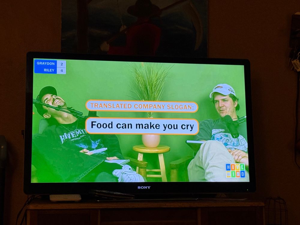 A photo of a TV showing a Hivemind Unlimited video with the text “translated company slogan: food can make you cry.”