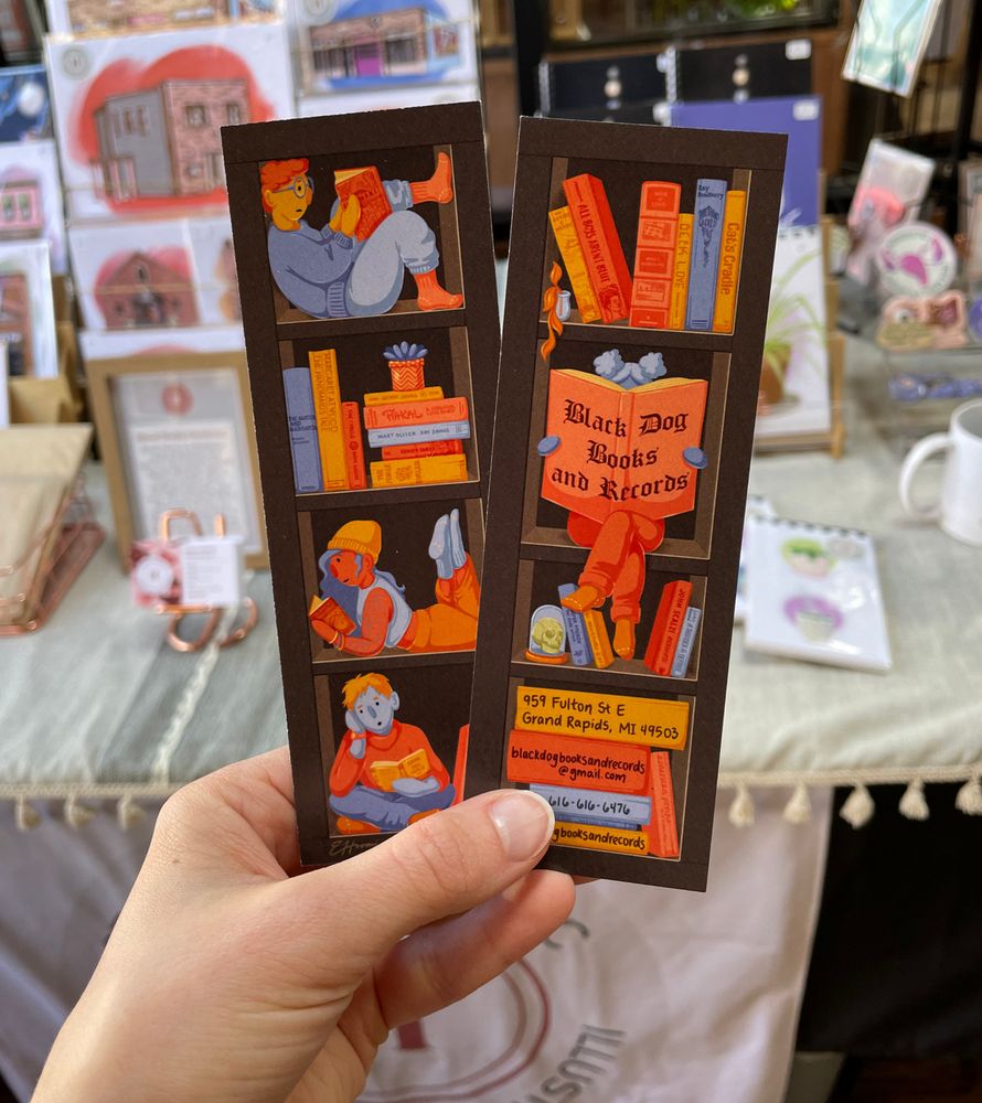 A photo of my hand holding up two of the bookmark I designed for Black Dog Books & Records in Grand Rapids, MI (showing the front and back). In the illustration both sides of the bookmark are framed within a bookshelf, where little characters are positioned in the shelves surrounded by books and other cozy props. The artwork is mostly a purple and orange color scheme, with simple character designs.

More project info:
I was given free rein to do whatever I wanted for this project, and from the start I imagined tiny characters inside of a bookshelf, surrounded by larger-than-life books. All of the books included in the artwork (aside from the ones containing the shop information) are real book spines--many of them banned or challenged books, a few others I chose, a few requested by the store owner, and some other random titles shouted out by friends as I was finishing the project.