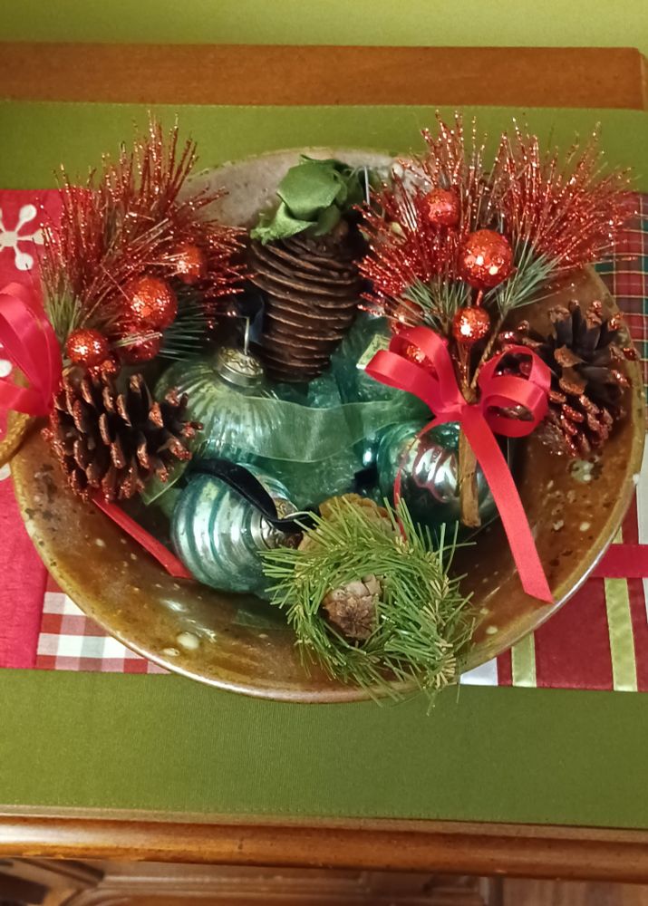 A bowl on a side bar with Christmas bulbs of green and pine cones and greenery filling it up.