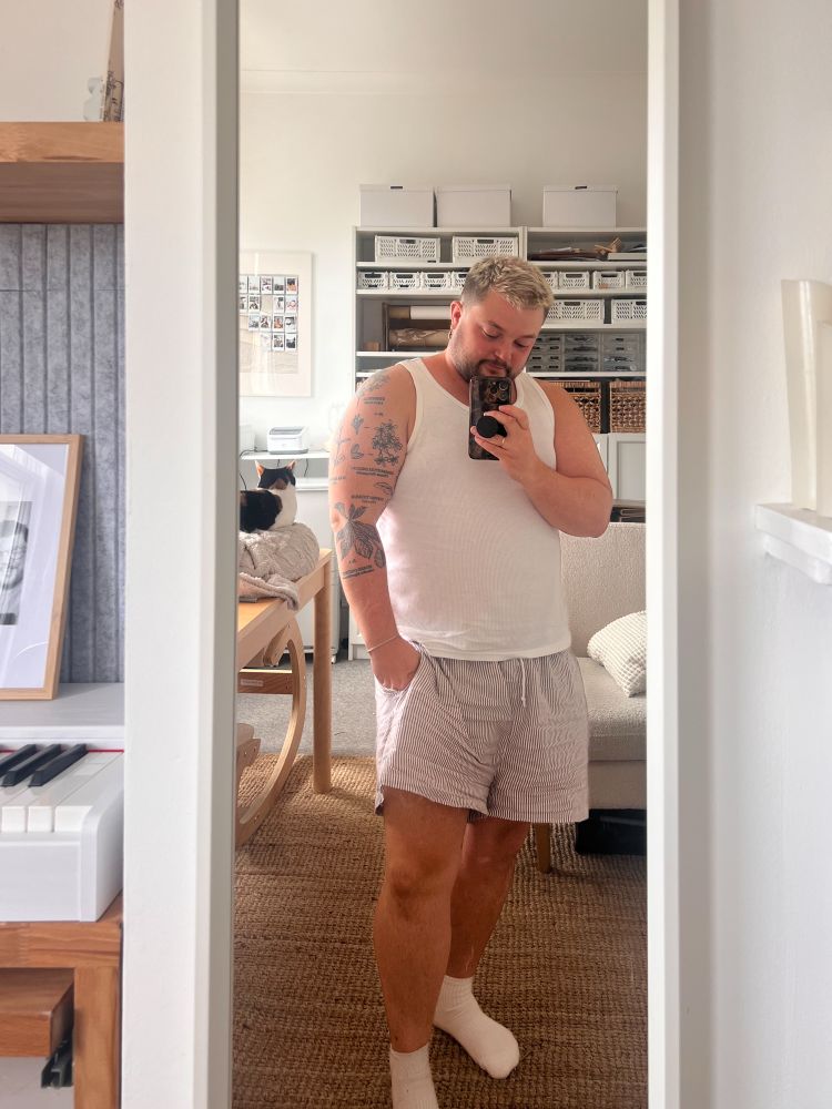 Ocean is standing in front of a mirror with a white vest and brown and white striped boxer shorts 