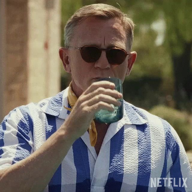 a man wearing sunglasses and a blue and white striped shirt is drinking from a glass .