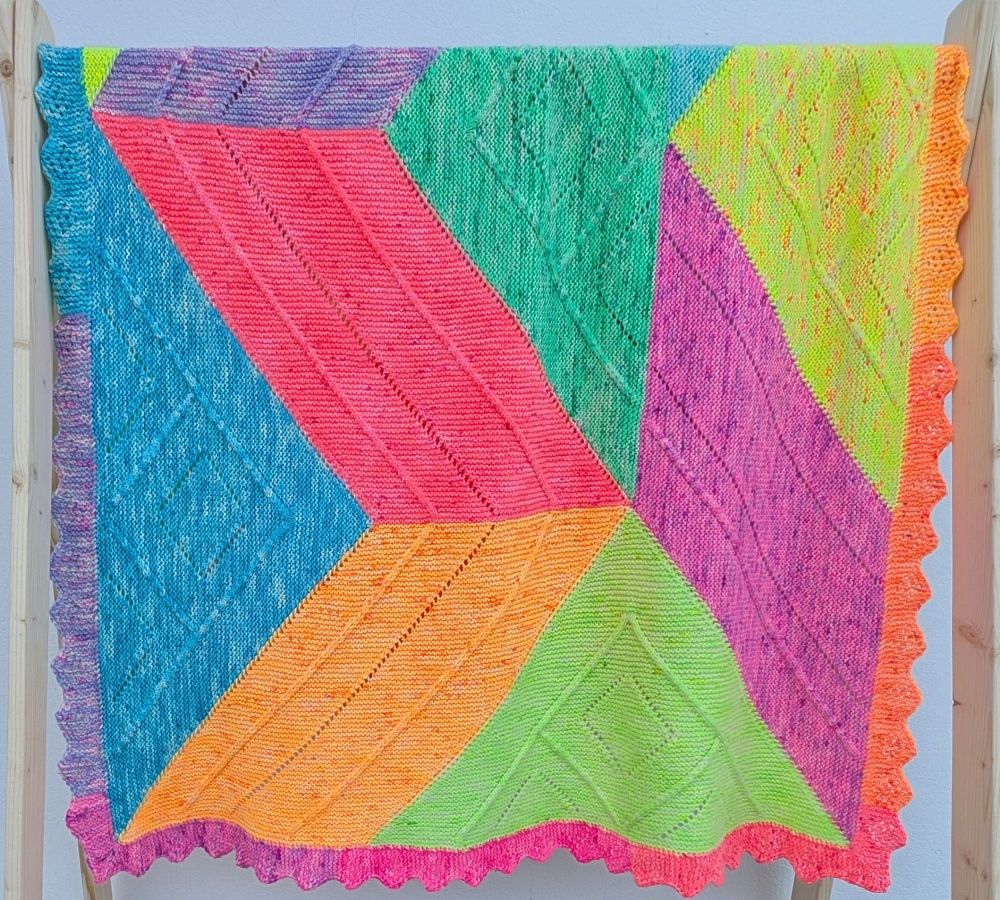 A blanket knit with many bright colours, hanging over a rod.