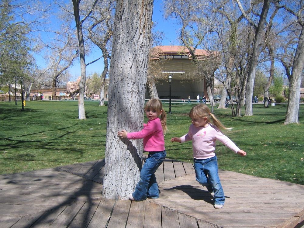 Twin girls running around a tree