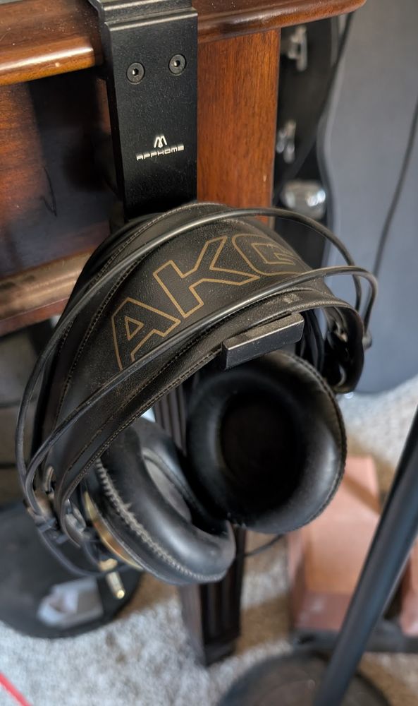 AKG headphones on a headphone hook. Desk and microphone stand in background. 