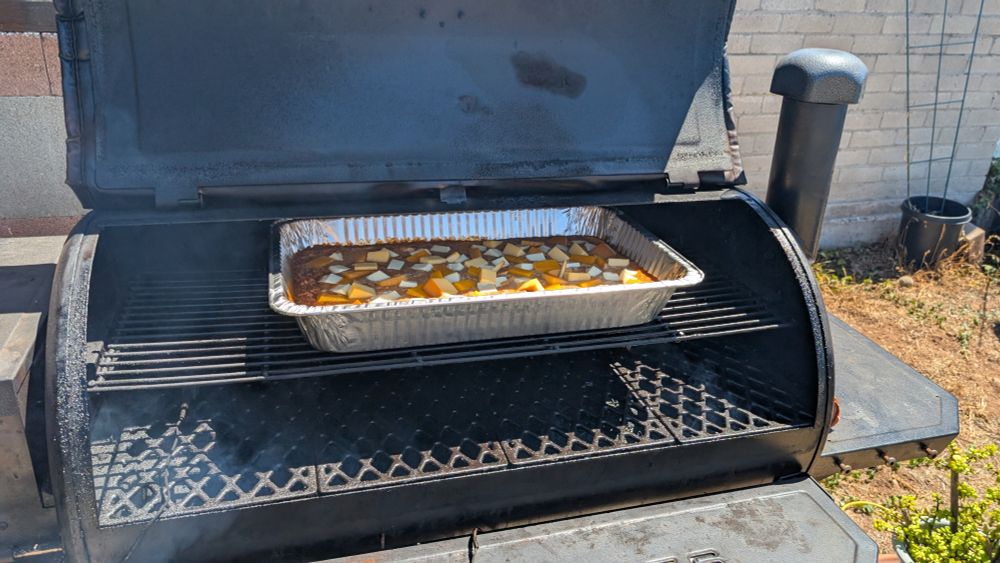 An aluminum pan filled with queso dip, inside of a pellet smoker.
