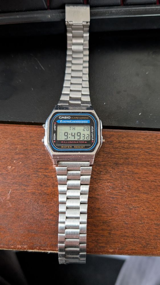Casio digital wrist watch. Silver color wrist watch with LCD face. Words Casio, Alarm Chrono, ElectroLuminescence, Light, Mode, Illuminator, Water Resist, Start/Stop appear on the face.