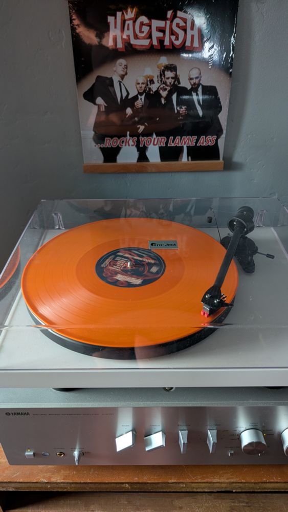 An orange record album on a record player. The cover art is above. Four men in black suits. Text reads "Hagfish ... Rocks your lame ass"