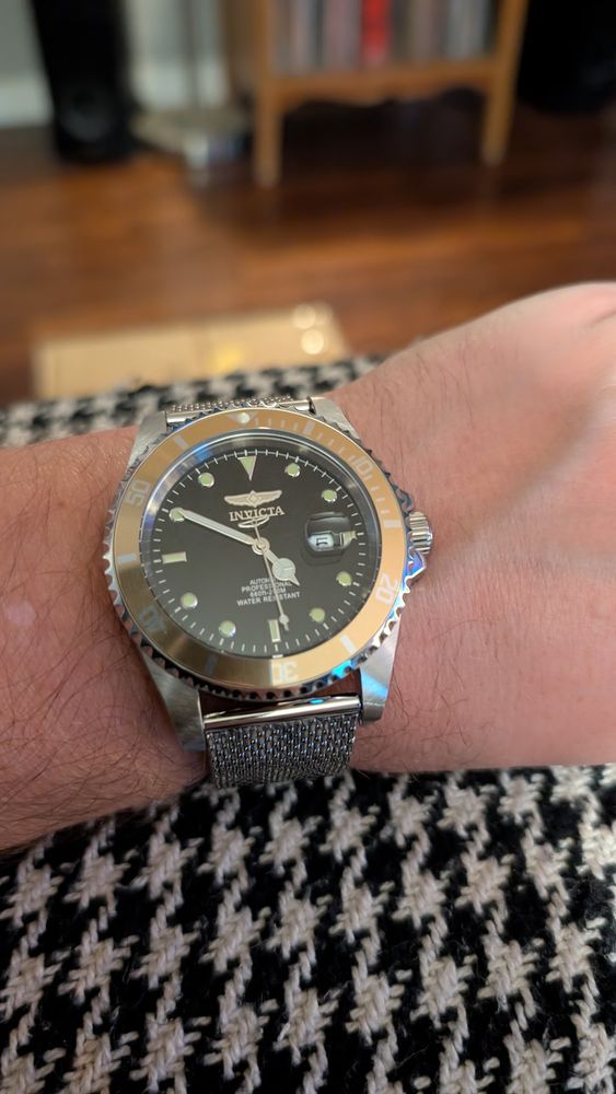 Wrist watch with a brass bezel and a silver braided metal strap, on a wrist. 