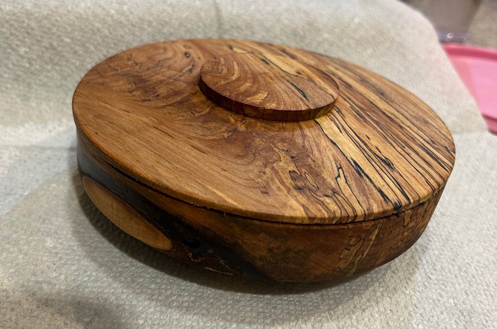 A turned wooden box with a shallow lid. There are black streaks (spalting) from fungal rot and dark blue epoxy fill. 