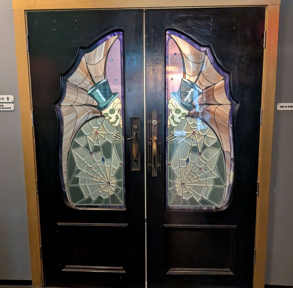 A pair of doors with a stained glass skeleton magician on them.