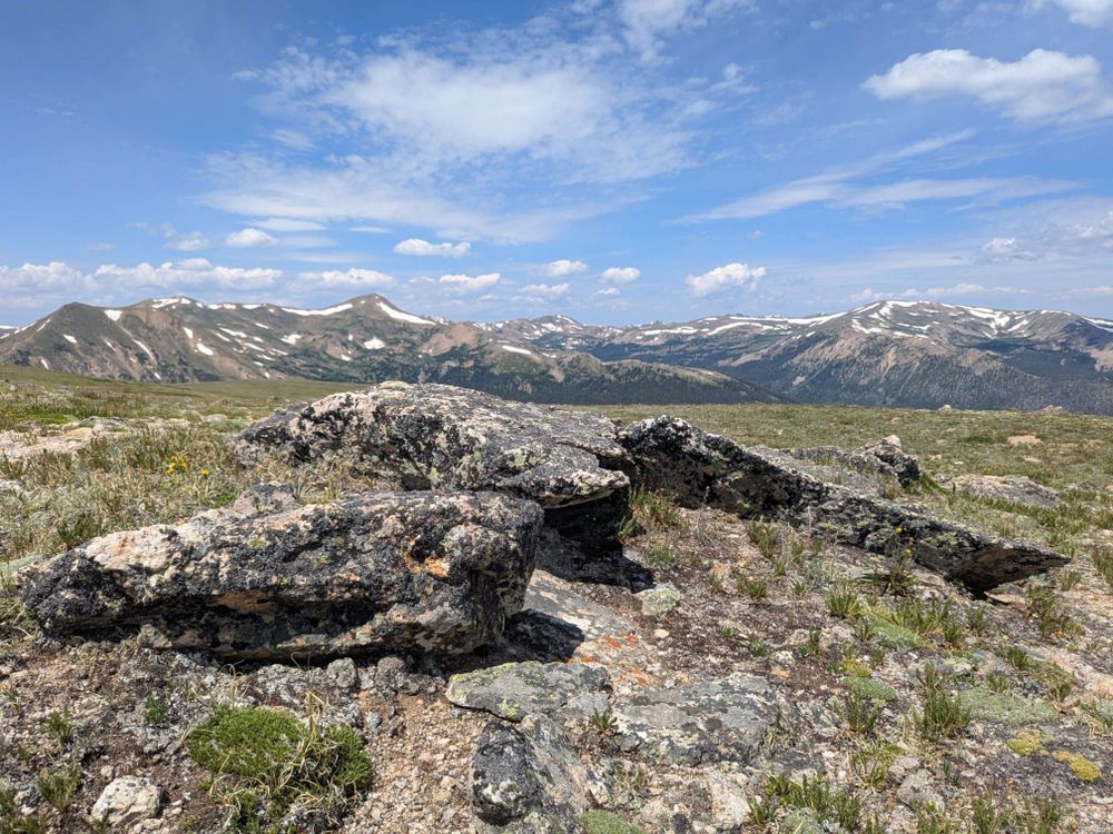 A set of mountain peaks forming a ridge in the background with alpine scrubland and rocks in the foreground.