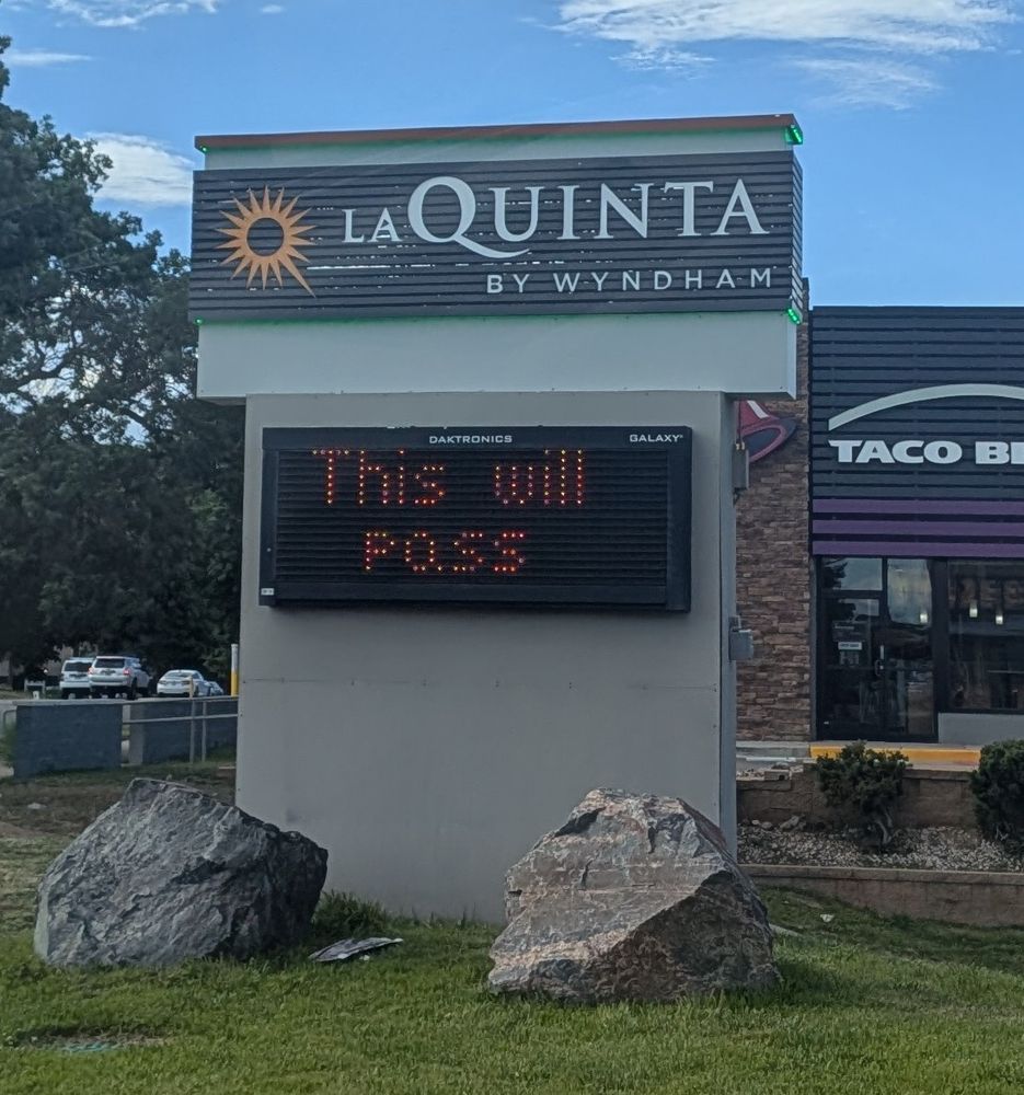A roadside sign for a La Quinta hotel with an LED panel that simply reads "This will pass"