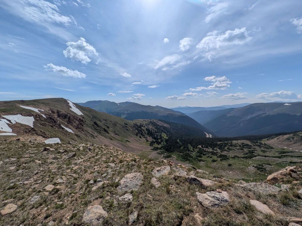 A wide angle view of a forested mountain valley from on top of a ridge.