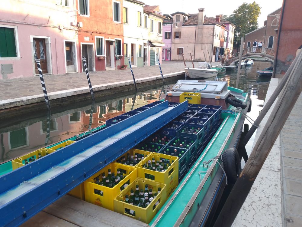 A boat in a canal filled with empty glass drinking water bottles in crates.