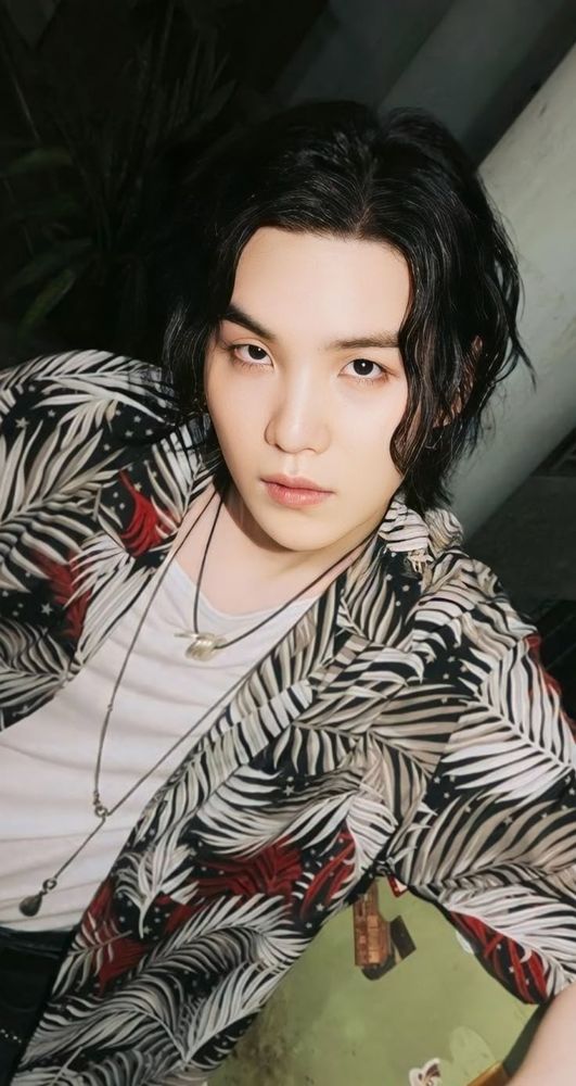 Yoongi on the set of Haegeum, with a slight curl to his hair, a white t-shirt, a dress shirt with a leaves print, and two necklaces.