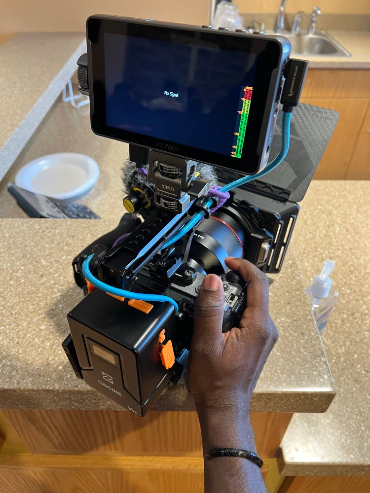 Hand of a black person holding camera rig with a battery, top handle, monitor and matte box