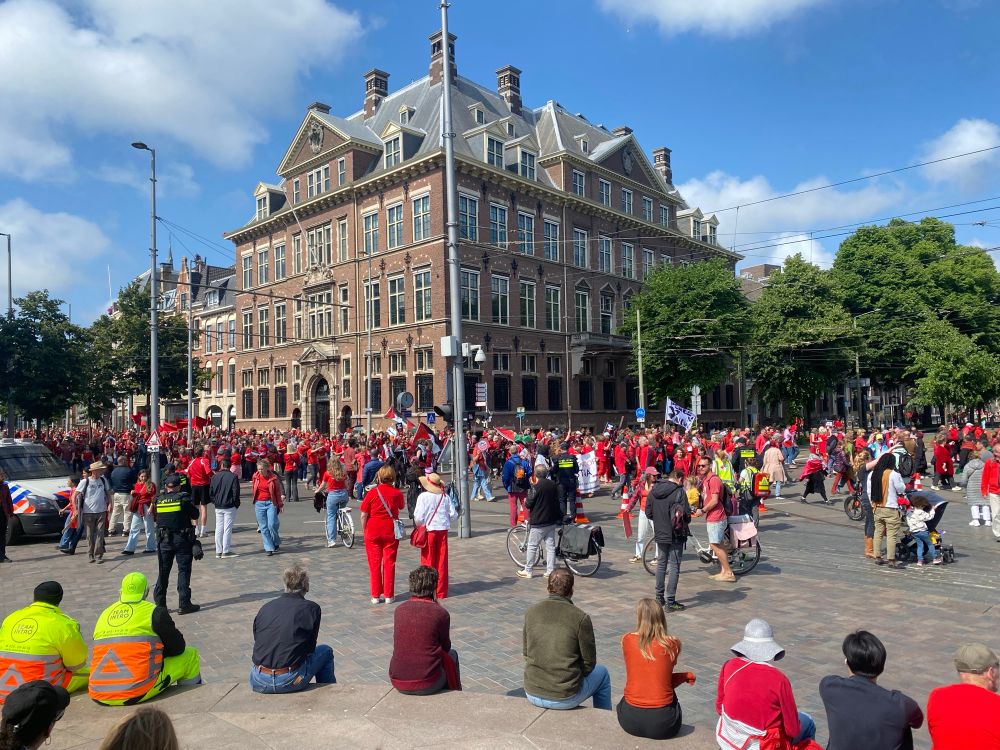 Passing crowd of protesters near Binnenhof and people watching them. 