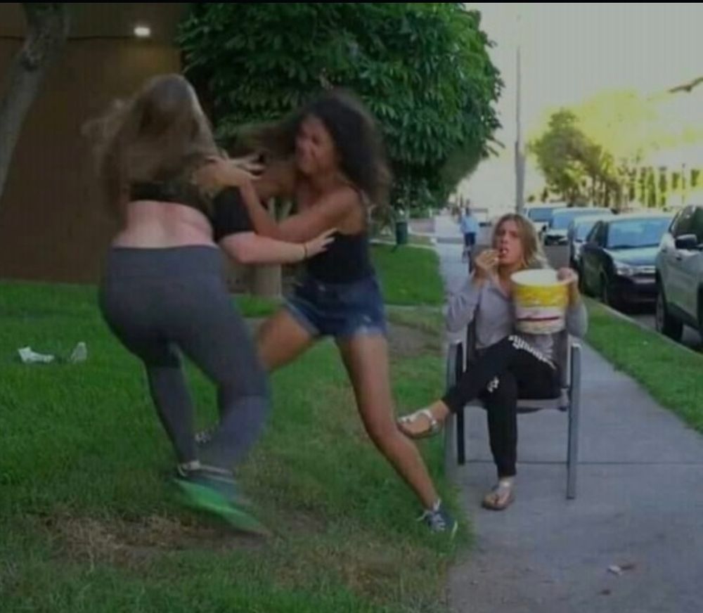 Two girls fighting. A third girl is watching while eating a huge tub of popcorn 🍿 