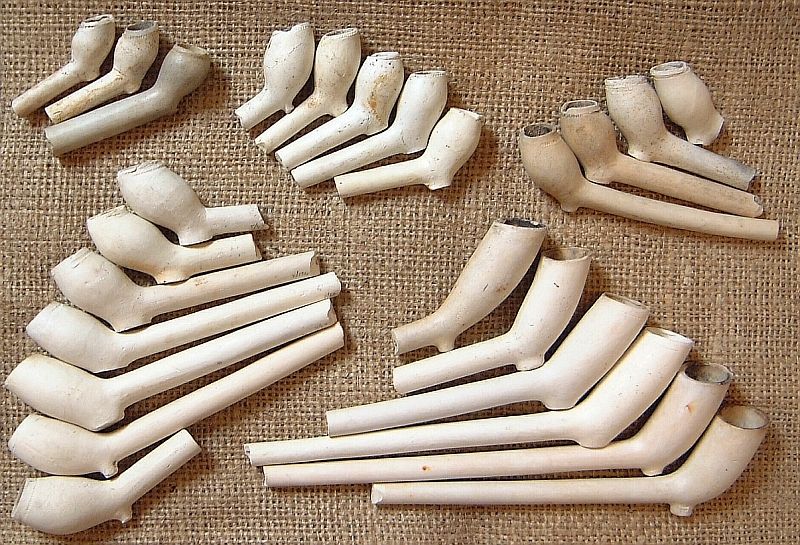 Discarded, white-clay smoking pipes, many with broken stems, likely from the early eighteenth century.