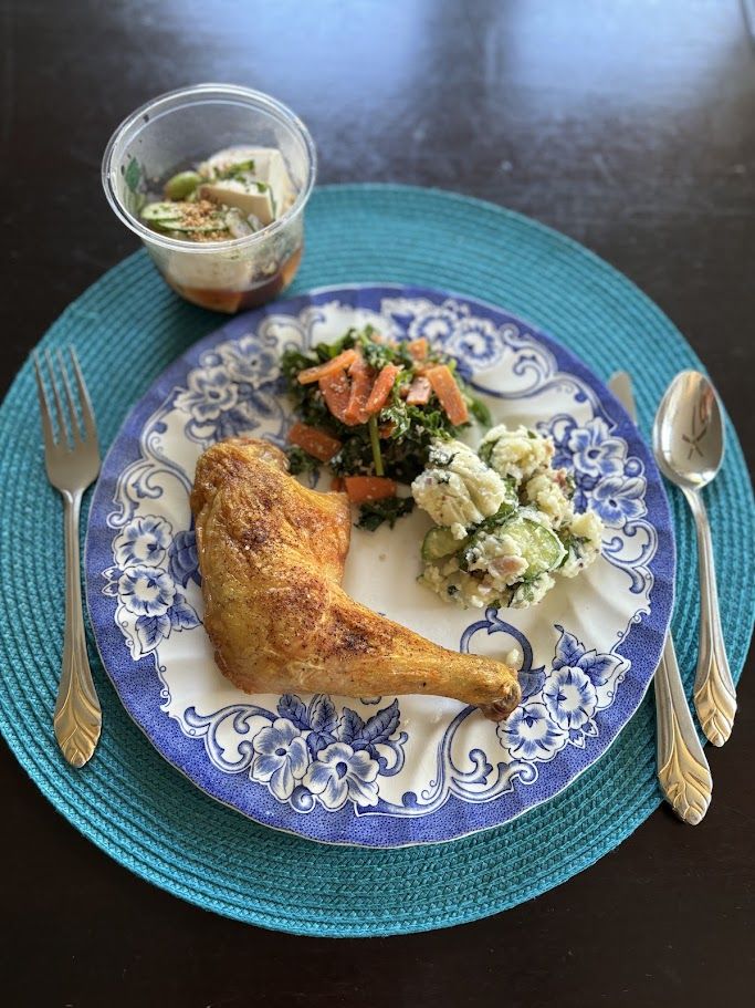 お皿に盛った骨付き鶏モモ肉、ポテトサラダ、ケールと人参の胡麻ポン酢和え、カップに入った冷ややっこ