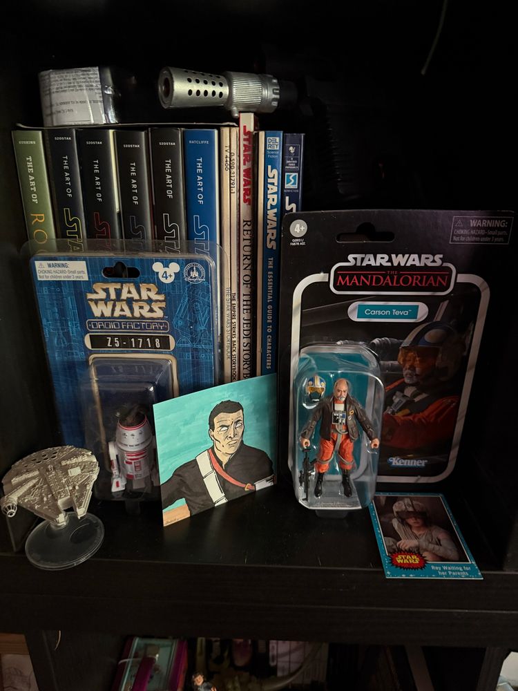 A small shelf filled with Star Wars books, art, trading cards, and toys.