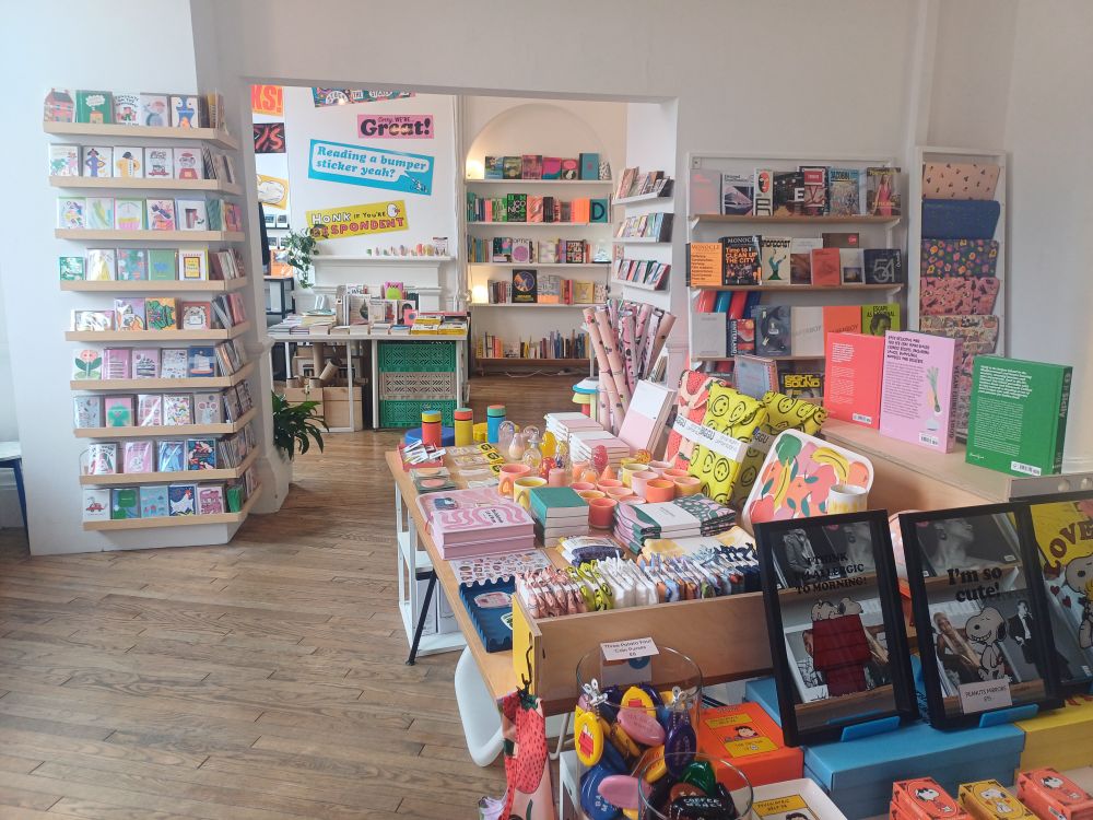 Photo of the interior of a shop with tables and shelves covered in bright coloured books and stationery.