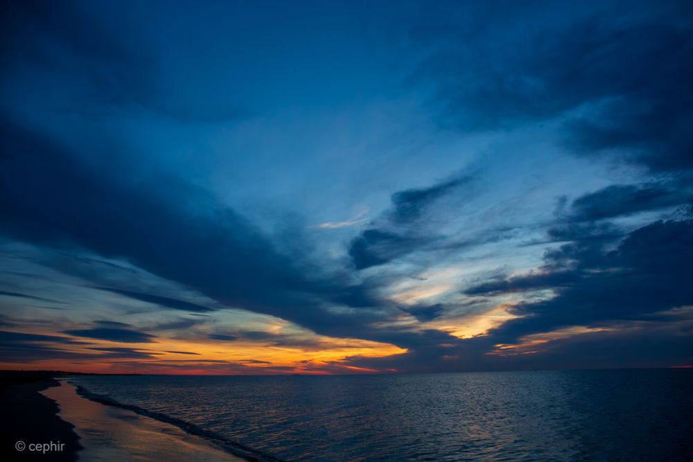 Sonnenaufgang über dem Meer. Der Himmel ist überwiegend dunkelblau, nur am Horizont ist schon oranges Licht zu sehen.