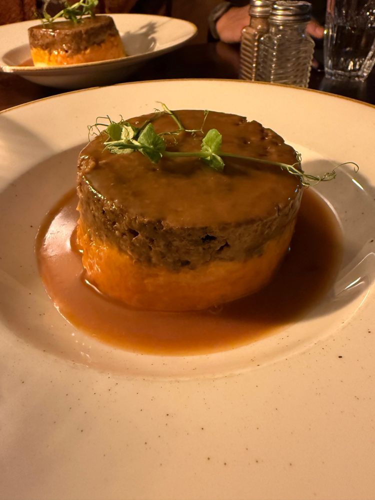 A plate of haggis atop mashed turnips and potatoes in a gravy. 